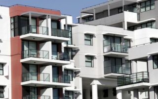 Modern apartment buildings with multiple balconies and large windows, featuring a mix of white and red exterior walls under a clear sky.