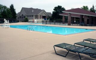 Outdoor swimming pool with a lifeguard chair, lounge chairs, and a clubhouse in the background on a cloudy day.