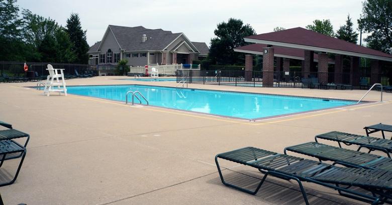 Outdoor swimming pool with a lifeguard chair, lounge chairs, and a clubhouse in the background on a cloudy day.