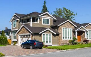 A modern two-story suburban house with a double garage, brick and siding exterior, manicured lawn, and a black car parked in the driveway.
