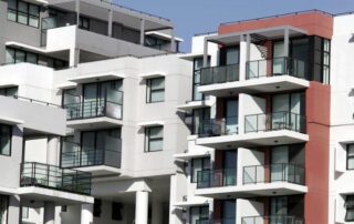 Modern apartment buildings with multiple balconies and large windows, featuring white and red exterior walls against a clear blue sky.