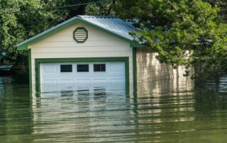 A garage partially submerged in floodwater, with water reaching more than halfway up the doors and trees surrounding the building.
