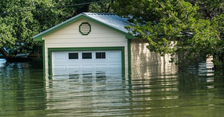 A garage partially submerged in floodwater, with water reaching more than halfway up the doors and trees surrounding the building.