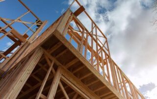 Timber framing of a building under construction, viewed from below against a partly cloudy sky.