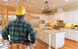 A construction worker in a hard hat stands in a partially built house, visualizing a finished kitchen with white cabinets and granite countertops.