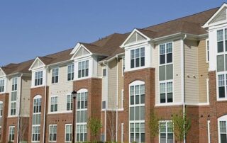 A row of modern, three-story apartment buildings with brick and beige siding exteriors under a clear blue sky.
