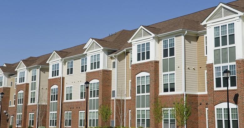 A row of modern, three-story apartment buildings with brick and beige siding exteriors under a clear blue sky.