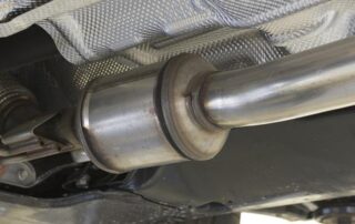 Close-up view of a car’s catalytic converter and exhaust pipe mounted underneath a vehicle.