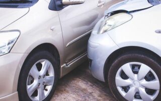 Two silver cars involved in a minor collision, with the front of one car touching the side of the other, showing visible dents and damage.