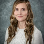 Portrait of a young woman with long wavy blonde hair and a light gray sweater.
